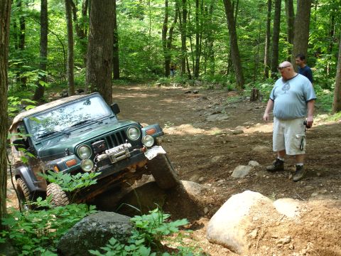 1996 Ford Bronco - Jeep Wrangler navigating a difficult off-road obstacle in a wooded area.