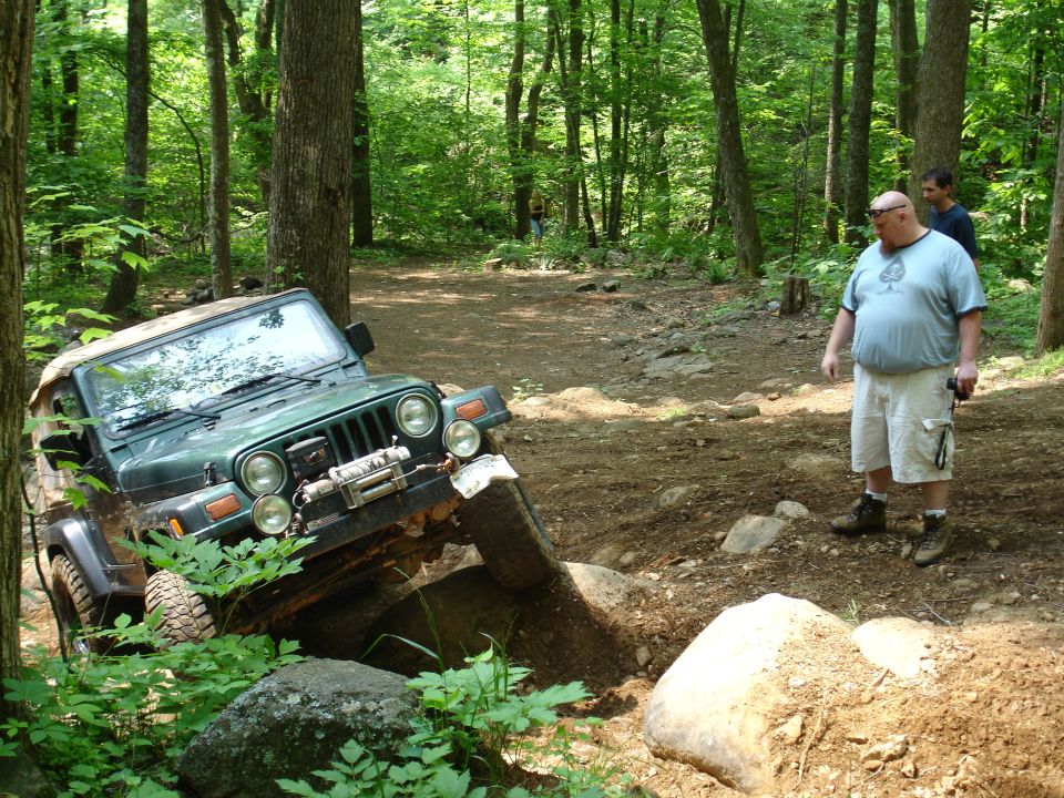 Green Jeep Wrangler climbing over rocks on a dirt trail in a forest