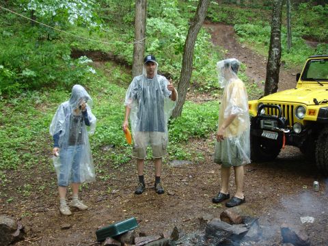 1996 Ford Bronco - A yellow Jeep Wrangler is parked in a wooded area with three people wearing ponchos.