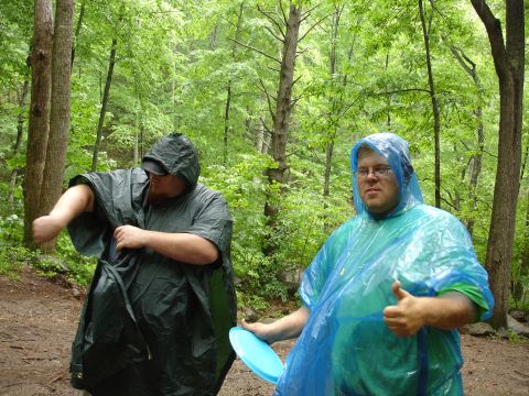 1996 Ford Bronco - Two men in ponchos are in a forest, one giving a thumbs up while holding a frisbee.