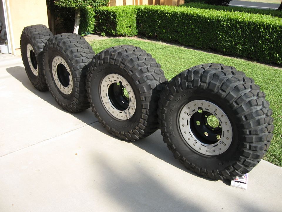 Four off-road mud tires on black beadlock wheels lined up on a driveway