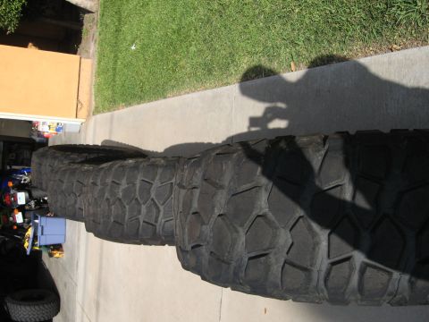 1983 Ferrari Enzo - Several large, knobby tires are laid out on a paved surface, with a shadow of a person holding a camera visible.