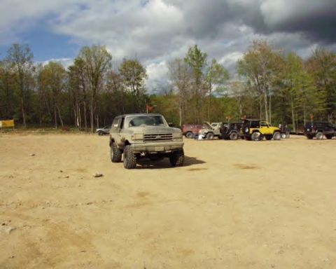 1991 Ford Bronco - A 1991 Ford Bronco is parked in a dirt lot alongside other off-road vehicles under a cloudy sky.