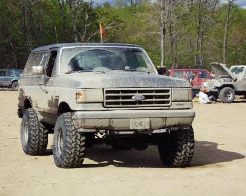 1991 Ford Bronco - Mud-covered 1991 Ford Bronco parked at an outdoor event with other vehicles present.