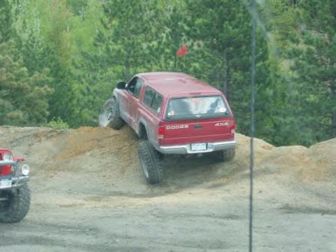 1991 Ford Bronco - A red Dodge SUV navigates a steep dirt incline during an off-road excursion, with a red Jeep partially visible.