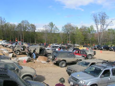 1991 Ford Bronco - A variety of off-road vehicles are gathered in a dirt lot, suggesting an event or meetup for enthusiasts.