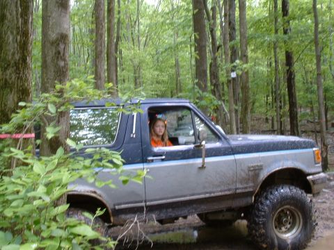 1991 Ford Bronco - A young girl is behind the wheel of a lifted Ford Bronco as it navigates a muddy, wooded path.