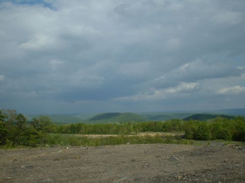 1991 Ford Bronco - A wide landscape view under a dramatic sky, with rolling green hills in the distance.