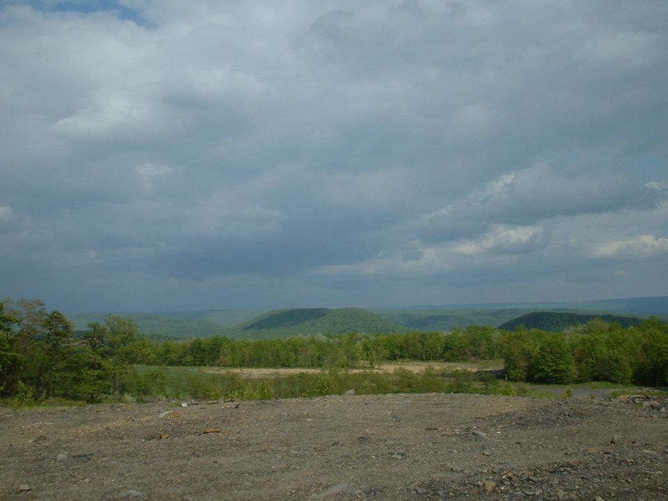 Dirt foreground with distant green hills and cloudy sky
