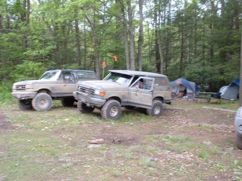 1991 Ford Bronco - Two 1991 Ford Broncos are parked at a campsite, with tents and trees visible in the background.