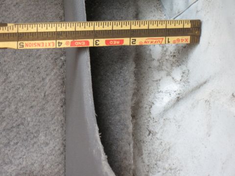 1994 Ford Bronco - A Lufkin X46 folding wooden ruler laid across a gap being measured between gray interior trim and carpeted panels, with a dusty white fiber…