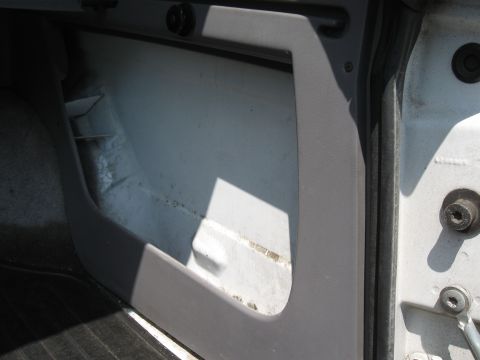 1994 Ford Bronco - Close-up of a gray plastic interior kick-panel or lower B-pillar trim piece with a large cut-out opening, revealing the white painted body…