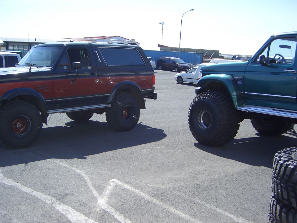 Two lifted Ford Broncos with big off-road tires parked in a lot.