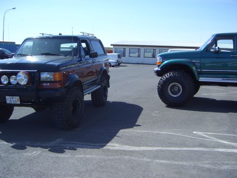 1996 Ford Bronco - Two Ford Broncos, one black and one green, are parked side-by-side in an outdoor lot.