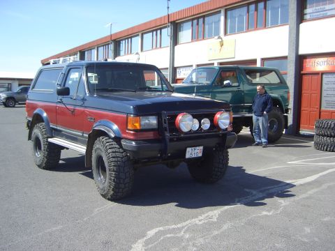 1996 Ford Bronco - A modified Ford Bronco with a two-tone paint job and large tires is parked outside a building.