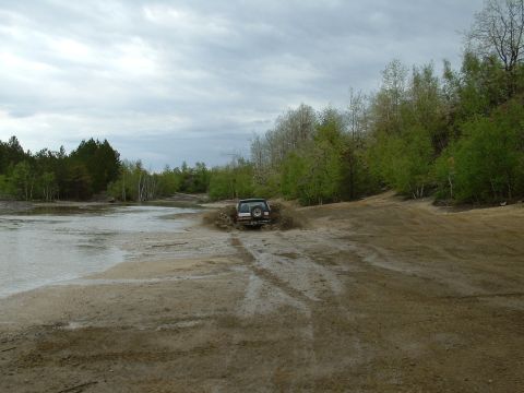 1991 Ford Bronco - An SUV navigates a challenging off-road course, splashing through mud and water under an overcast sky.