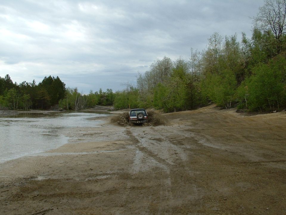 SUV kicking up mud and water while driving through a muddy area with trees and a cloudy sky