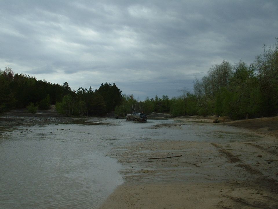 SUV driving through shallow water with trees in background