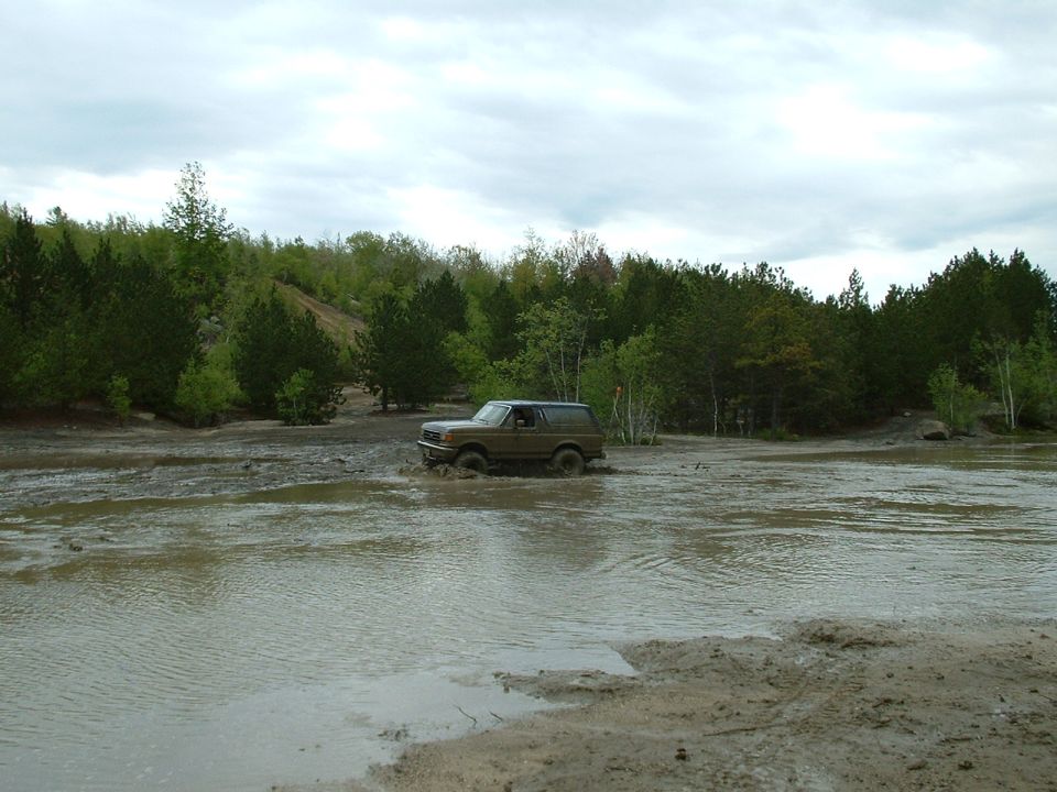 Brown 1991 Ford Bronco driving through a muddy field