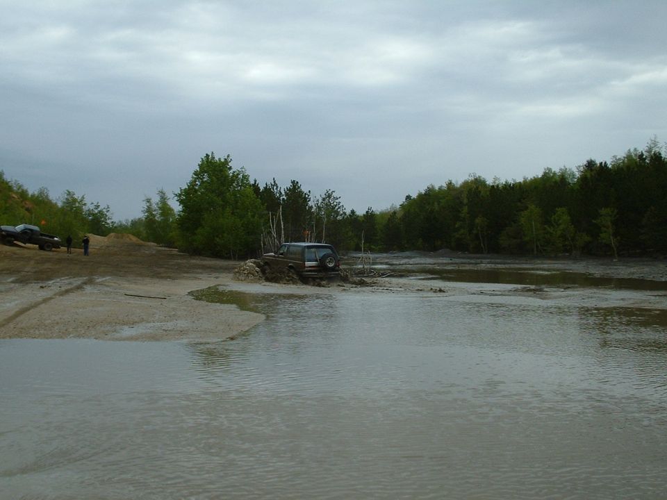 Off-road vehicles navigating a muddy, watery terrain with trees in the background