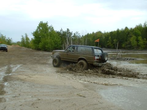 1991 Ford Bronco - A Ford Bronco navigates a challenging muddy terrain, kicking up spray as it goes.