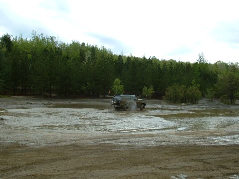 1991 Ford Bronco - A 1991 Ford Bronco navigates a muddy terrain, kicking up water and dirt.