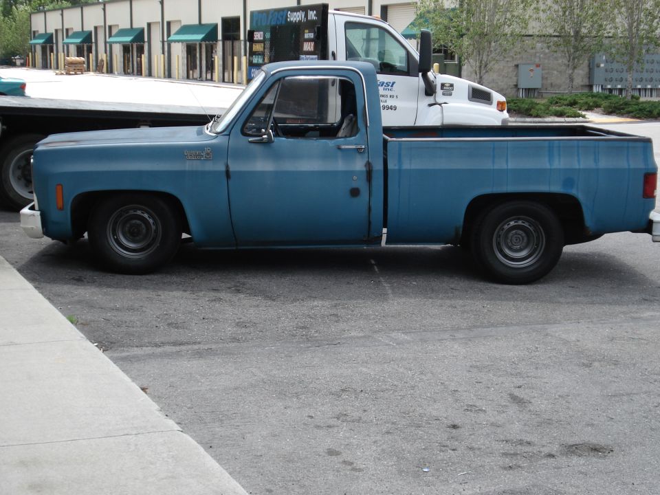 Side view of a lowered blue Chevrolet C10 pickup with steel wheels parked in a lot