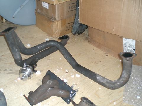 1995 Ford Probe - Exhaust components, including a manifold and pipes with a wastegate, are laid out on a floor near cardboard boxes.