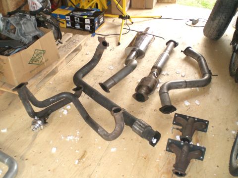 1995 Ford Probe - Various exhaust system parts are displayed on a wooden surface, possibly for a vehicle repair or upgrade.