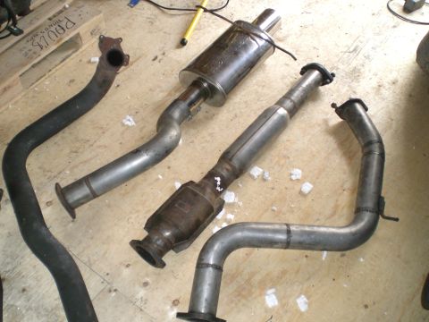 1995 Ford Probe - Several exhaust system components, including a muffler and catalytic converter, are displayed on a workshop floor.