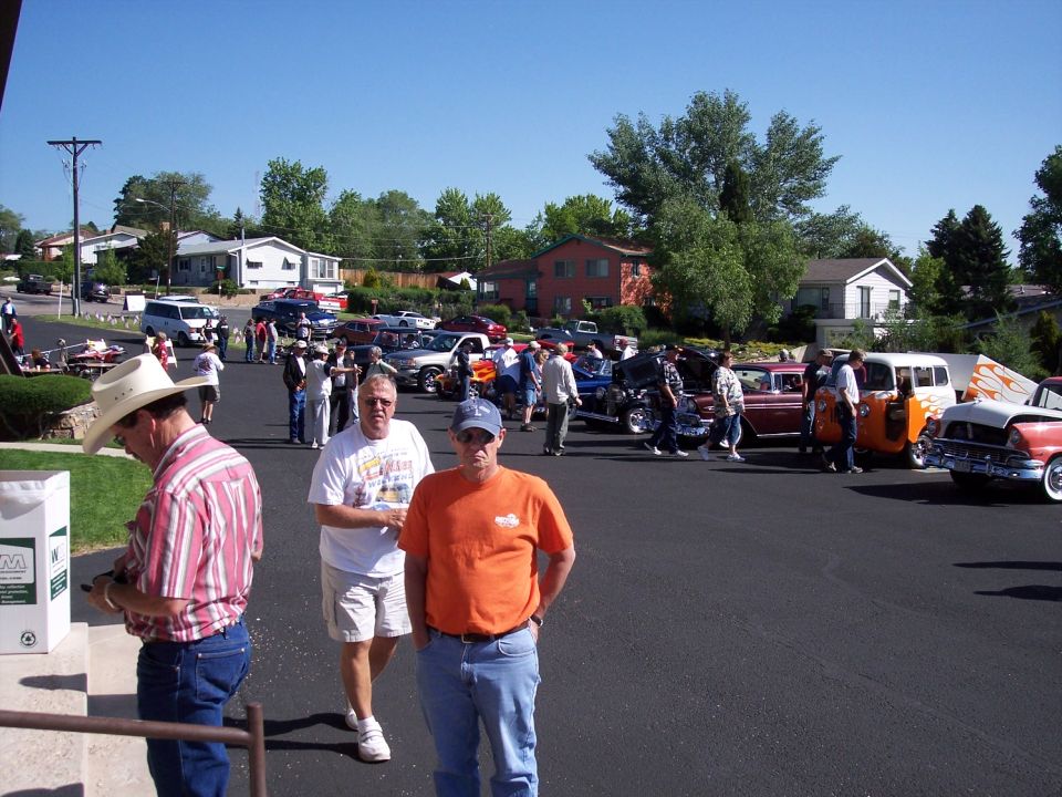 Several classic cars parked on asphalt, some with hoods open, under a clear blue sky