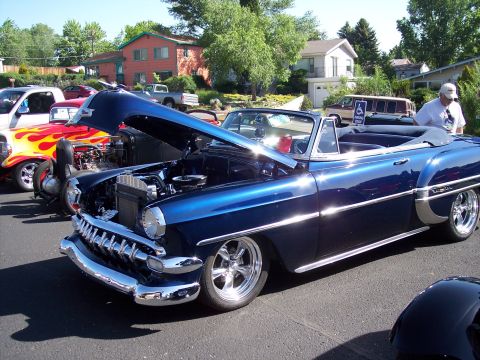 1972 Ford Ranchero - A blue 1953 Chevrolet Bel Air convertible is parked at a car show, hood up, next to a red hot rod.
