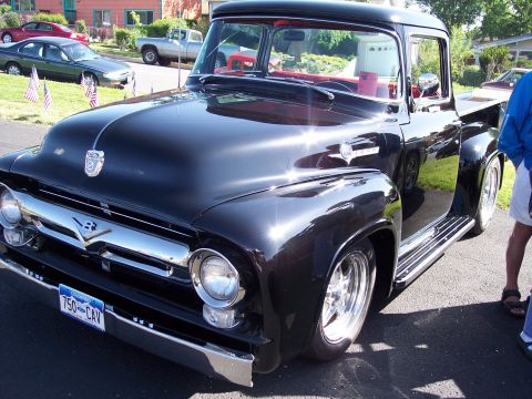 1972 Ford Ranchero - This black 1956 Ford F-100 pickup truck is parked on a street with other vehicles visible in the background.