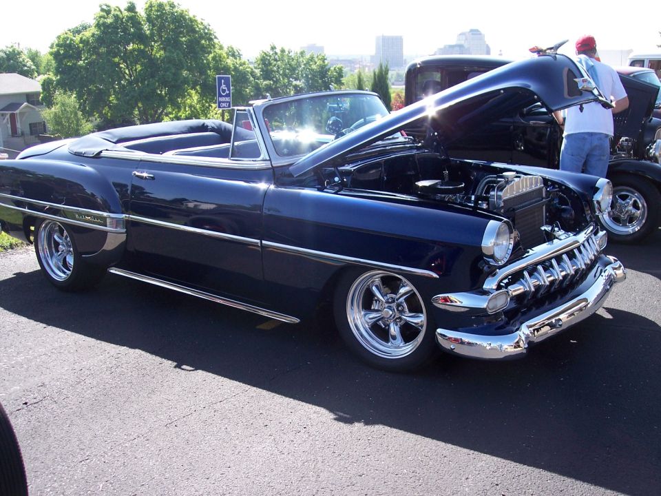 Dark blue convertible with chrome grille, hood open, and custom wheels