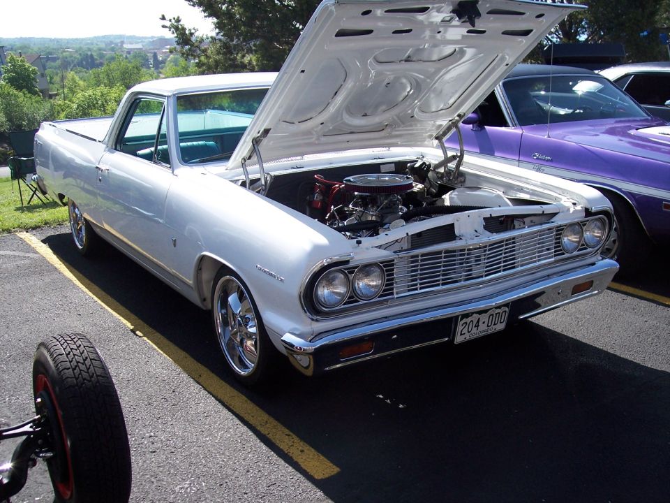 White 1964 Ford Ranchero with hood open, chrome wheels, and a purple car behind it