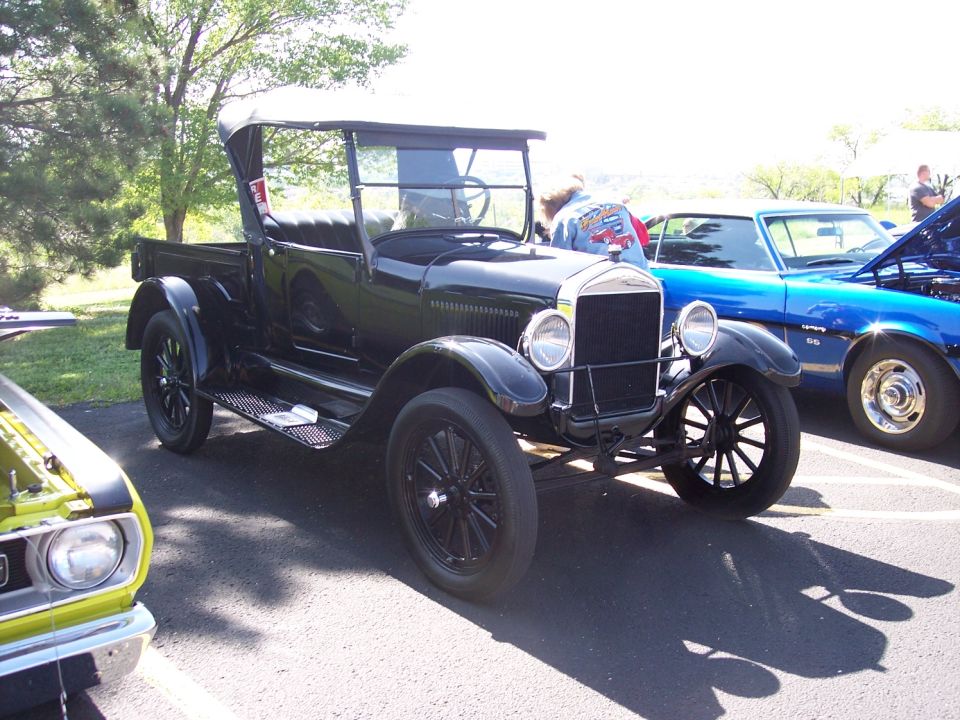 Old dark-colored truck with a canvas top, parked outside. Another car is to the right