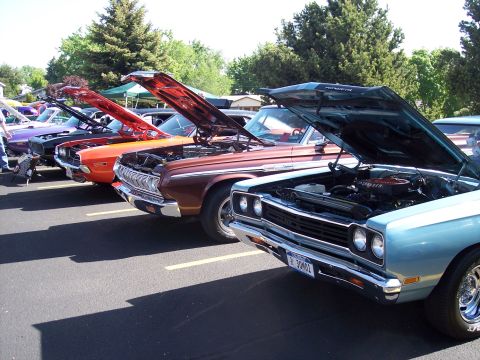 1972 Ford Ranchero - A line of cars, including a light blue 1972 Ford Ranchero with its hood open, are parked outdoors at an event.