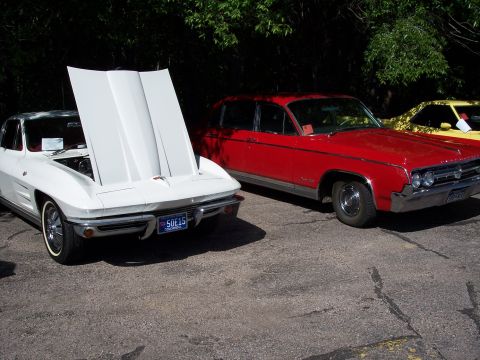 1972 Ford Ranchero - A white 1963 Chevrolet Corvette is parked next to a red sedan, with the Corvette's hood raised.