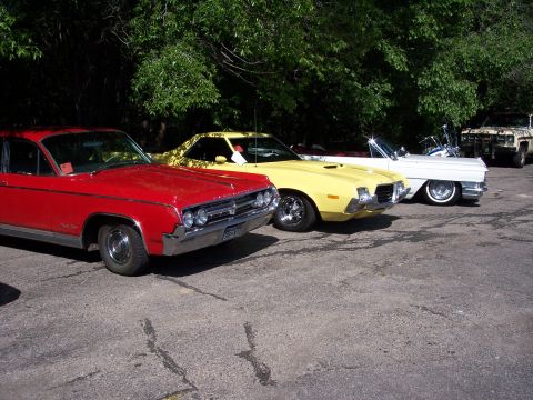 1972 Ford Ranchero - A line of classic cars includes a yellow 1972 Ford Ranchero parked behind a red car.