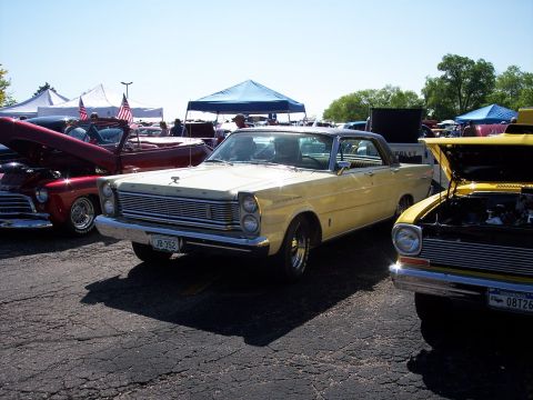 1972 Ford Ranchero - A yellow 1965 Ford coupe is parked at an outdoor car show with other vehicles.
