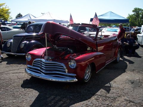 1972 Ford Ranchero - A classic red convertible is displayed with its hood open, alongside other vehicles at an outdoor event.