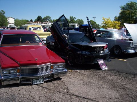 1972 Ford Ranchero - A modified black car with distinctive doors and an open hood is displayed at an outdoor event.