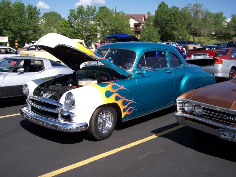 1972 Ford Ranchero - A custom coupe with flame graphics and its hood up is parked at an outdoor event.