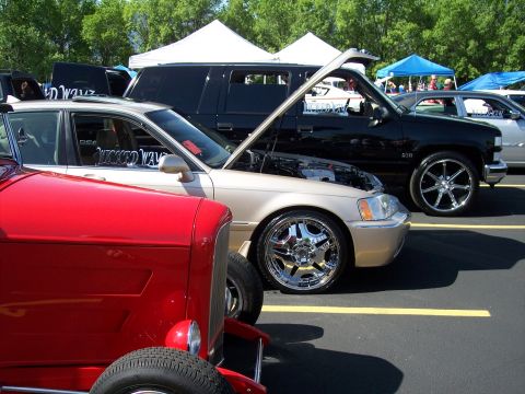 1972 Ford Ranchero - A tan sedan with its hood open is parked at an outdoor event, displaying custom wheels and a decal on the window.