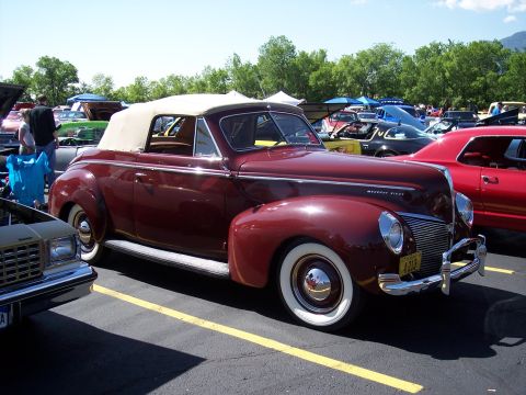 1972 Ford Ranchero - A classic maroon convertible is displayed at an outdoor car show with other vehicles in the background.