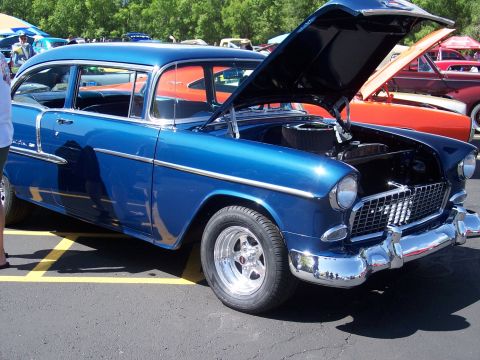 1972 Ford Ranchero - Blue 1955 Chevrolet sedan, hood up, at a car show with other vehicles present.