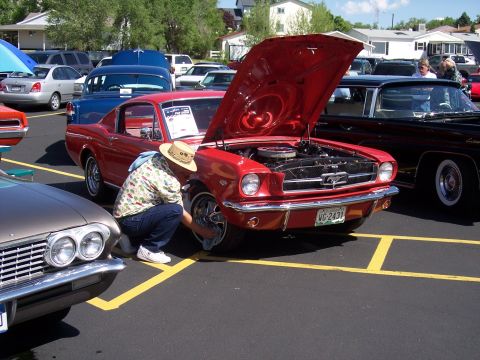 1972 Ford Ranchero - A person cleans the front wheel of a red 1965 Ford Mustang coupe at a car show, with other vehicles visible in the background.