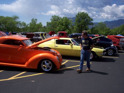 1972 Ford Ranchero - Several custom cars are parked in a lot under a cloudy sky, with a man observing them.