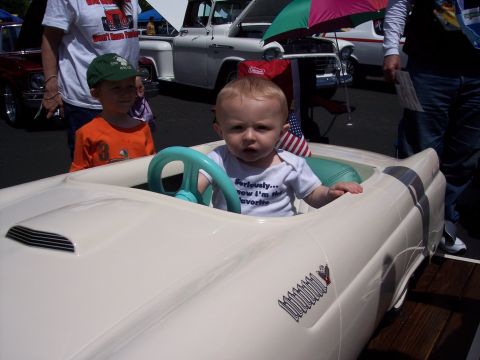 1972 Ford Ranchero - A baby is playing in a toy car at an outdoor event with other vehicles visible.