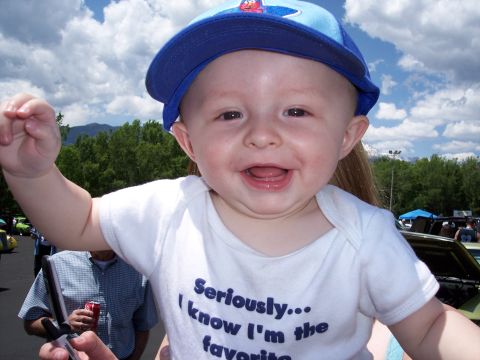 1972 Ford Ranchero - Smiling baby in a blue cap and white onesie at an outdoor event with cars in the background.